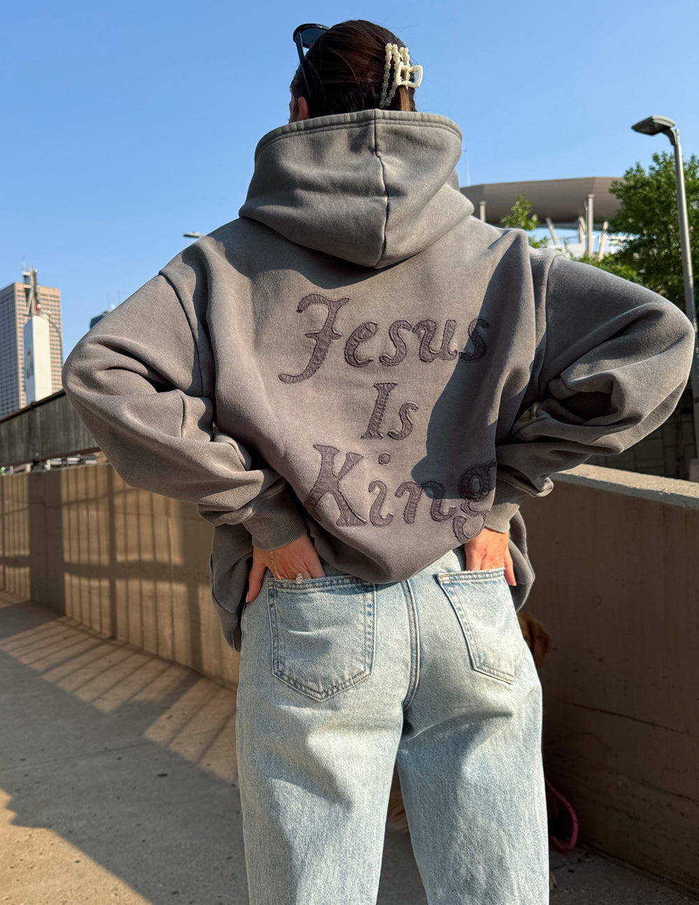Person wearing a grey Not Sorry Jesus Is King Unisex Hoodie with text on the back outdoors in sunlight
