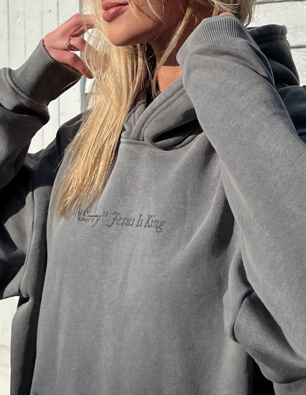 Woman wearing gray Not Sorry Jesus Is King Unisex Hoodie with subtle text on the chest in natural light.