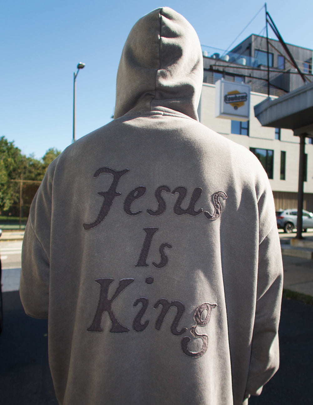 Person wearing gray Not Sorry Jesus Is King Unisex Hoodie with text "Jesus Is King" on the back outdoors in daylight