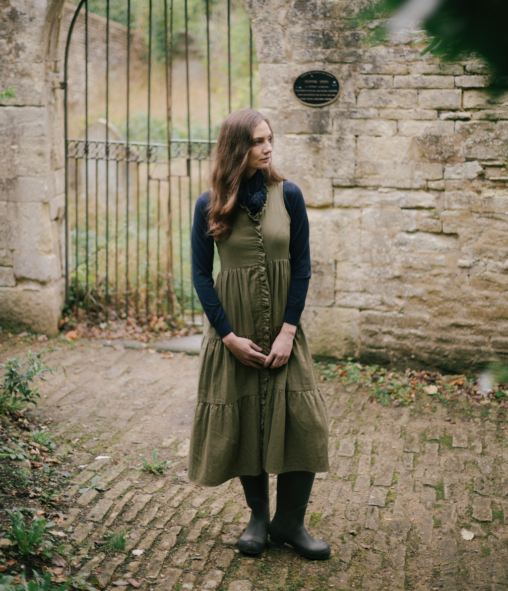 Woman wearing an olive green buttoned midi dress layered over a navy long-sleeve top with boots, called The House Dress.