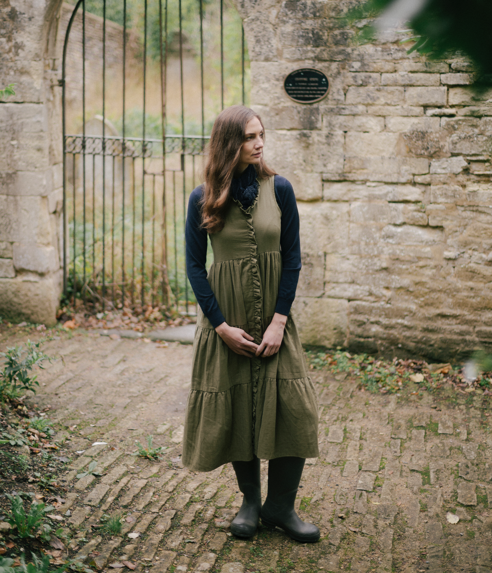 Woman wearing an olive green buttoned midi dress layered over a navy long-sleeve top with boots, called The House Dress.