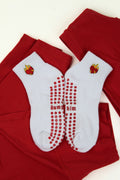 White Dump Him Grip Socks with red heart flame design and red anti-slip dots on soles, laid on red fabric background