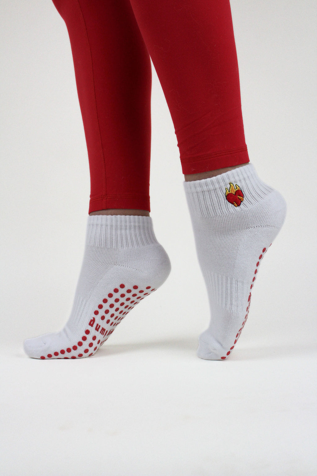 White ankle Dump Him Grip Socks with red non-slip dots and flame heart design worn with red leggings