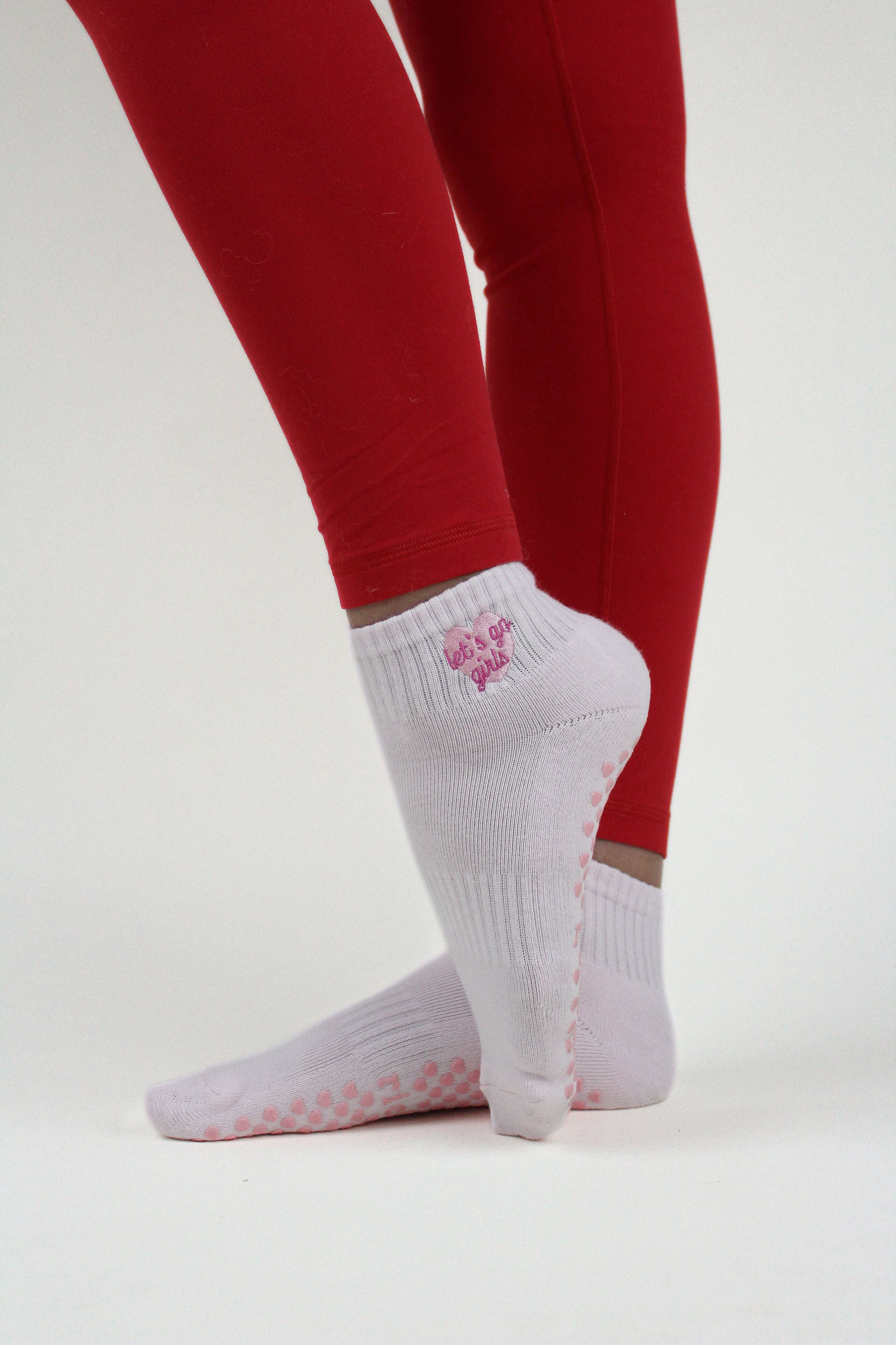 Feet wearing white PREORDER: Let's Go Girls Grip Socks with pink grips and red leggings on a white background