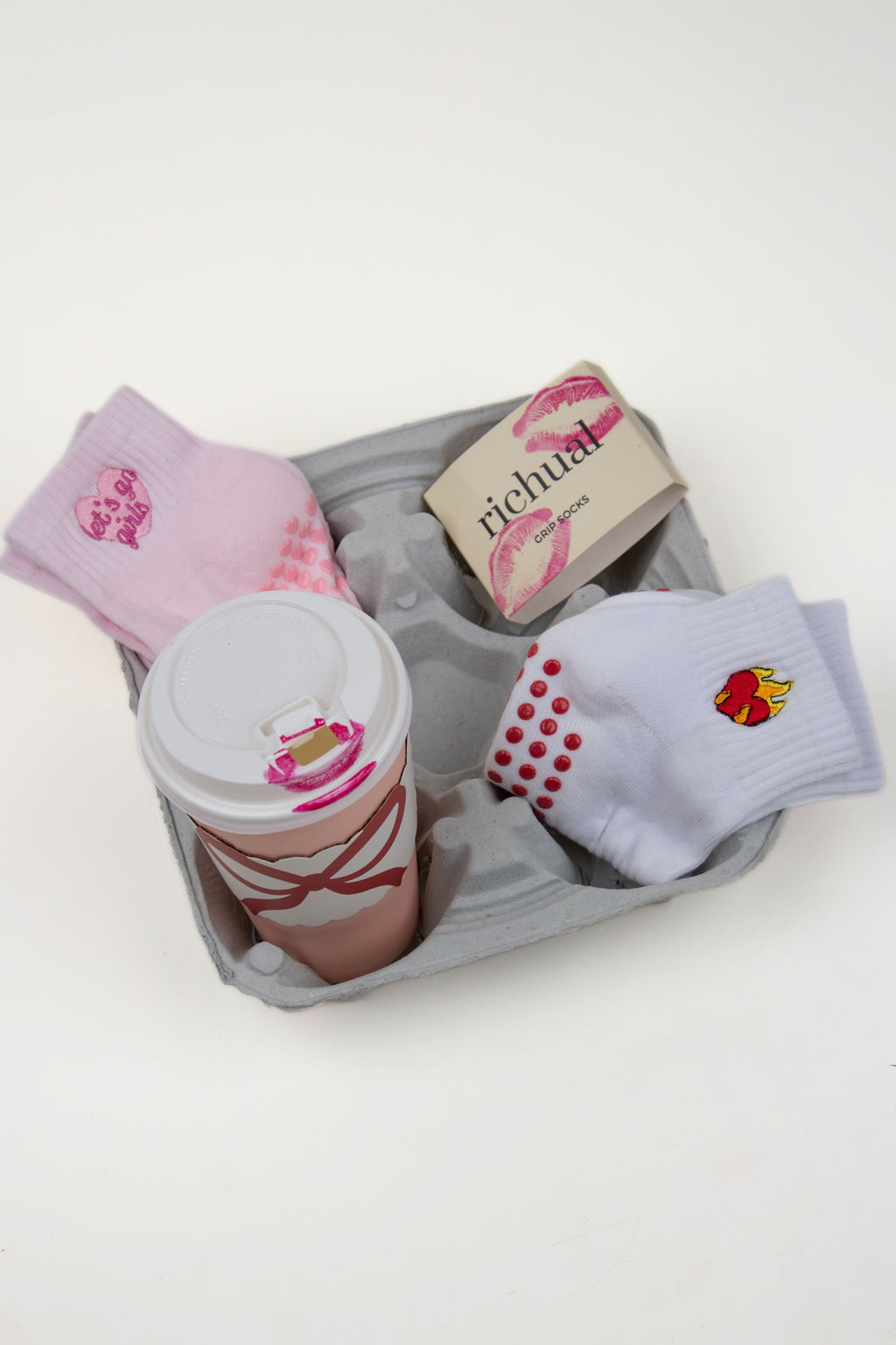 Dump Him Grip Socks in pink and white with grip dots and heart and flame designs in a gray tray with a coffee cup